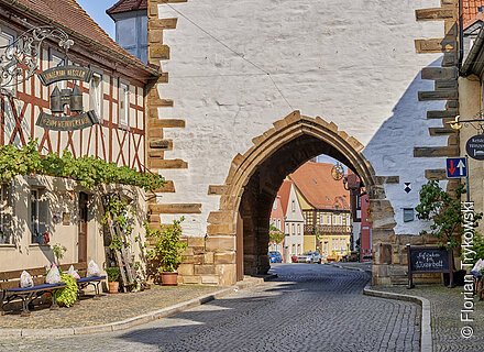 Ein mittelalterliches Stadttor, davor ein Fachwerkensemble.