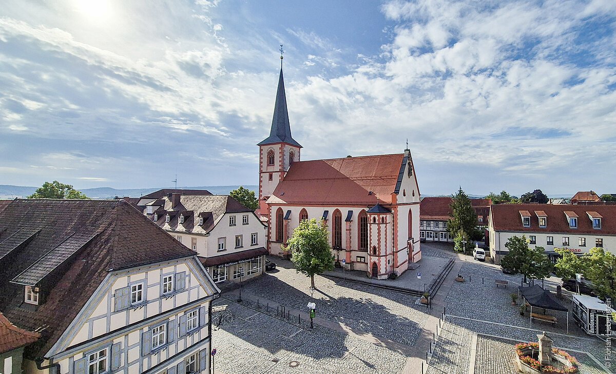 Historisches Gebäude mit Kirchturm auf einem gepflasterten Platz, umgeben von Fachwerkhäusern.